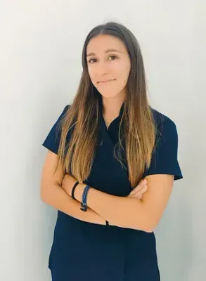 Una mujer con una blusa azul está de pie con los brazos cruzados.